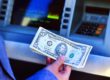 Hand holding cash in front of ATM