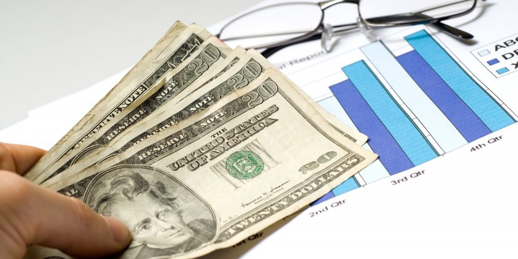A hand holding cash placed over graphs A hand holding cash placed over graphs