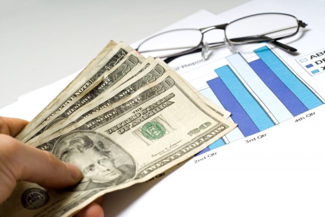 A hand holding cash placed over graphs A hand holding cash placed over graphs